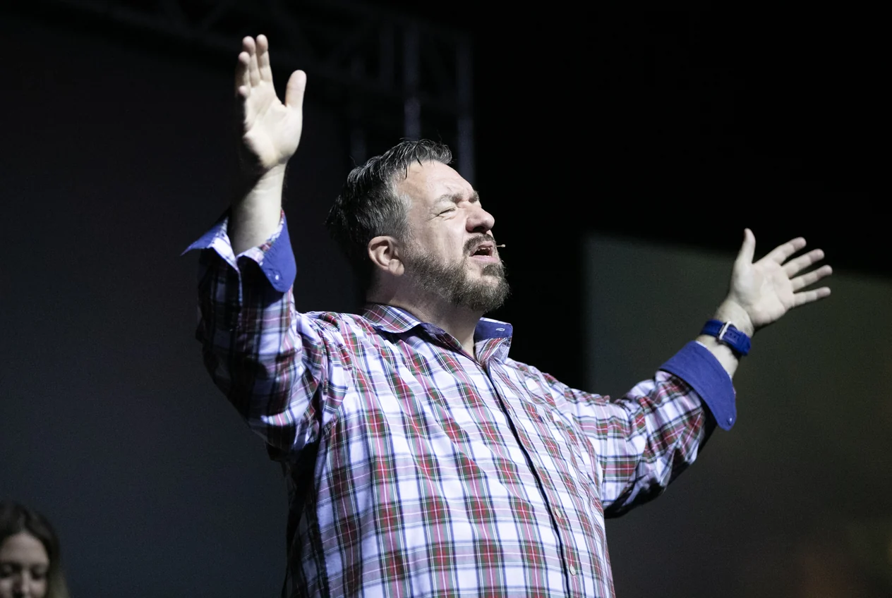 Lon Dean teaching on stage with both arms raised.